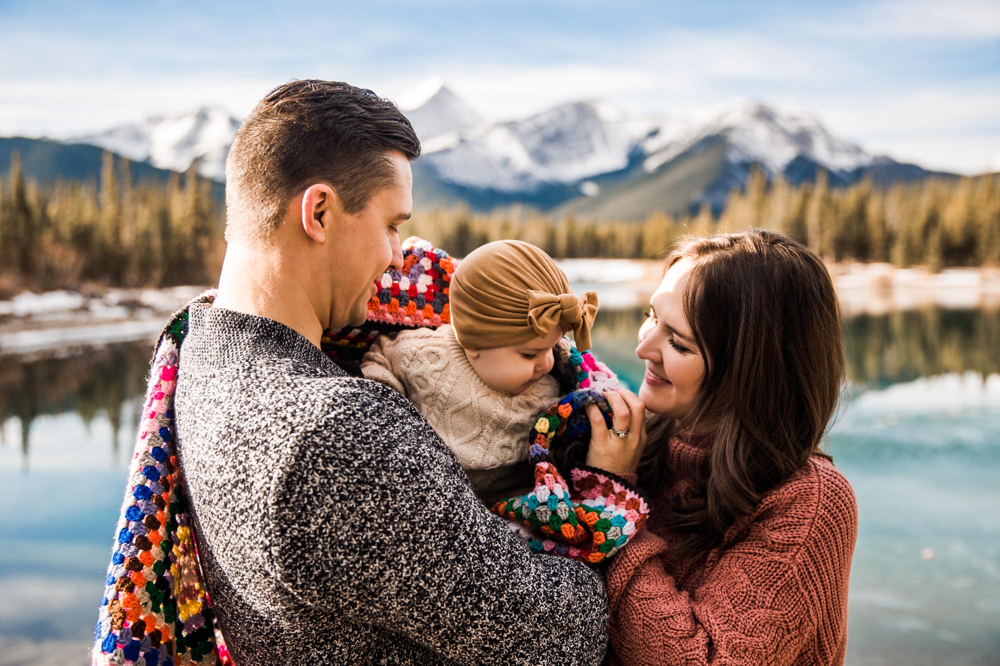 Calgary family photographer, family photos in the mountains in Kananaskis Country, parents with their baby in front of mountains and frozen water
