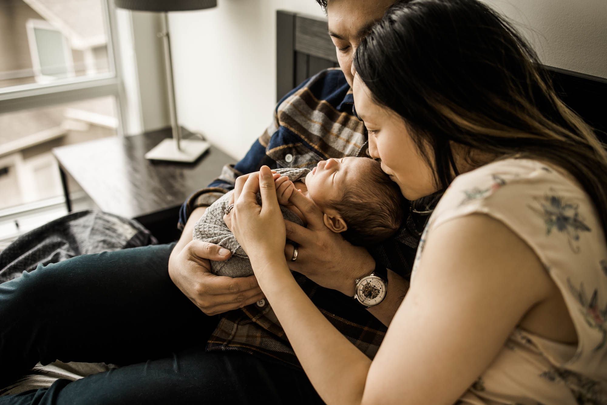 Calgary newborn and maternity lifestyle photographer, newborn baby in his parent's arms during an in-home lifestyle newborn photo session
